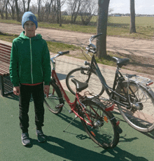 a boy in a green jacket is standing next to a red bicycle