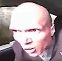 a close up of a bald man 's face in a car looking at the camera .