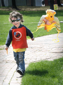 a young boy wearing sunglasses is flying a kite with a winnie the pooh balloon attached to it