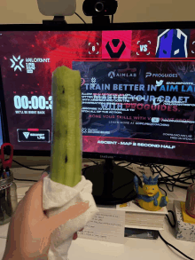 a person holding a green popsicle in front of a monitor that says valorant