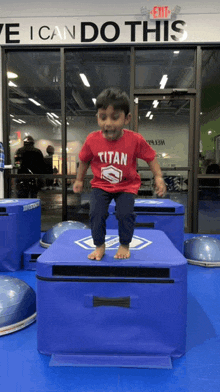 a young boy wearing a red shirt that says titan is jumping over a blue box