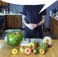 a man in a black shirt is standing in a kitchen surrounded by fruit and vegetables