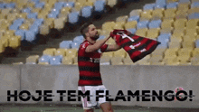 a soccer player is holding a flag in front of a stadium with the words hoje tem flamengo written on the bottom