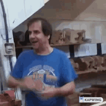 a man wearing a blue shirt is standing in a room with a lot of wood .