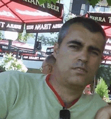 a man wearing sunglasses and a green shirt is sitting in front of a restaurant with red umbrellas .