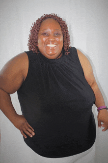 a woman wearing a black tank top is smiling with her hand on her hip