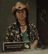 a woman wearing a cowboy hat is standing in front of a sign that says employees must wash hands before returning to work