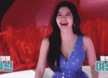 a woman in a blue dress is smiling in front of a red curtain