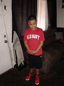 a young boy wearing a red old navy shirt stands in a living room