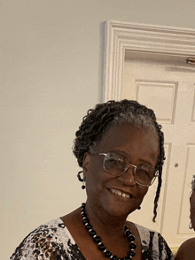 an older woman wearing glasses and a black necklace smiles for the camera