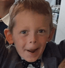 a young boy wearing a bow tie and a suit is smiling .