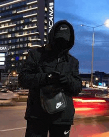 a man wearing a mask and a hat is standing in front of a building in a city .