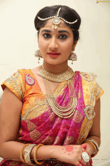 a woman wearing a pink saree and gold jewelry is standing in front of a wall