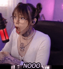 a woman with a tattoo on her chest is sitting in front of a microphone with the word nooo below her