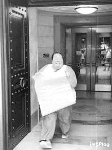 a black and white photo of a man holding a large piece of paper in front of a door that has a handicap sign on it