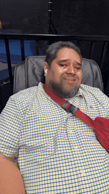 a man in a plaid shirt is laying in a chair with a red sling around his neck