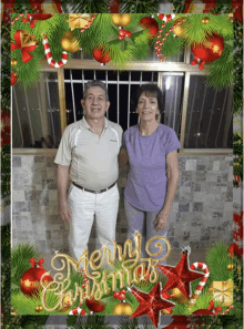 a man and woman are standing in front of a merry christmas sign