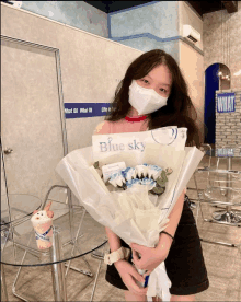 a woman wearing a mask holds a bouquet of flowers with a sign that says blue sky on it