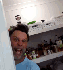 a man in a blue shirt is making a funny face in front of a pantry filled with bottles and jars