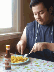 a man sitting at a table with a plate of food and a bottle of cole 's hot sauce in front of him