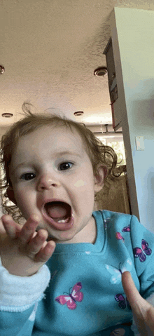 a baby in a blue shirt with butterflies on it is making a funny face