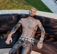 a shirtless man laying on a couch with a necklace around his neck