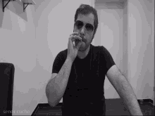 a man wearing sunglasses and a black shirt is smoking a cigarette in a black and white photo taken by senor cucho