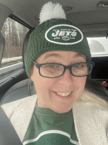 a woman wearing a jets hat and glasses smiles in a car