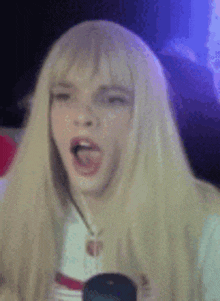 a woman wearing a blonde wig is making a funny face with her mouth open .