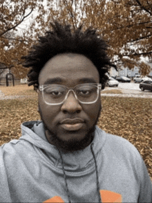 a man wearing glasses and a grey hoodie stands in front of a park