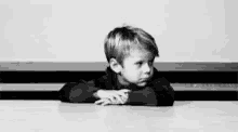 a black and white photo of a young boy sitting at a table with the words wow behind him .