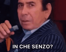 a man in a striped suit is holding a cell phone and asking in che senza