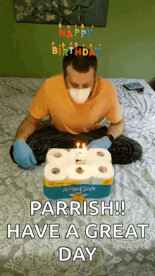 a man wearing a mask is sitting on a bed with a birthday cake made out of toilet paper rolls .