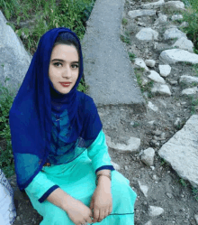 a woman wearing a blue hijab and a green dress sits on the ground