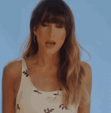 a woman wearing a white tank top with leaves on it is singing