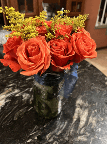 a mason jar filled with orange roses and yellow flowers on a counter