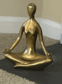 a gold statue of a woman sitting in a lotus position on a yoga mat