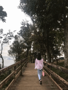 a woman walking down a wooden walkway with trees on both sides