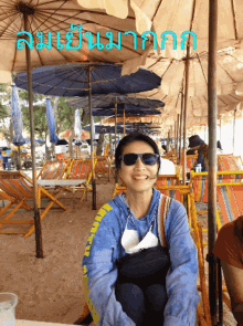 a woman wearing sunglasses sits under an umbrella on a beach in front of a row of chairs and umbrellas