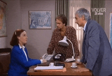 a woman is sitting at a desk talking to two men in a room .