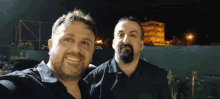 two men are posing for a picture at night and one has a beard