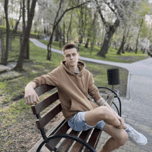 a young man in a brown hoodie sits on a wooden bench