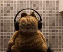 a stuffed cat wearing headphones in front of a tile wall