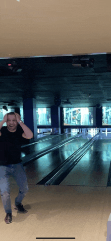 a man in a black shirt is standing in a bowling alley with his hands on his head