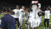 a group of soccer players celebrate on the field with a scoreboard in the background that says 52 to 13