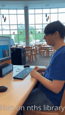 a man in a blue shirt sits at a desk in front of a computer with the words hop on nths library above him