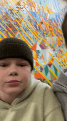 a boy wearing a beanie and a hoodie stands in front of a colorful wall