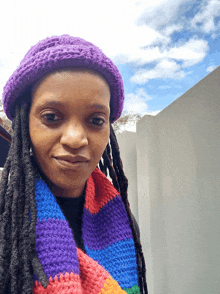 a woman wearing a purple hat and a rainbow scarf smiles for the camera