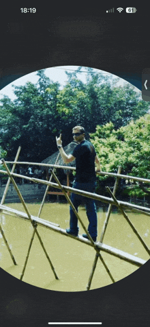 a phone screen shows a man standing on a bamboo bridge giving the middle finger