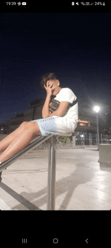 a person sitting on a railing with the time of 19:39 on their phone screen